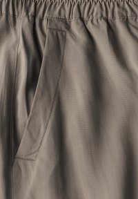 Bruine stof met een elastische tailleband, zijzak en een gladde textuur met subtiele plooien, die een ontspannen ontwerp en draping benadrukt.