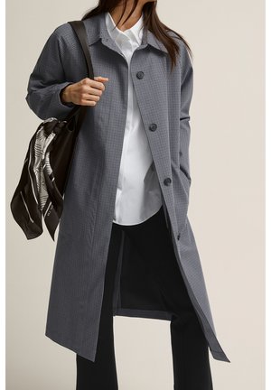 Cappotto lungo a quadri grigio con chiusura a bottone, colletto classico e vestibilità rilassata. Accompagnato da una borsa nera con una sciarpa fantasia.
