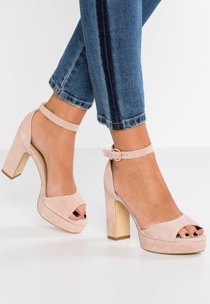 Jasnoróżowe sandały na wysokim obcasie z zamszu, z odkrytymi palcami, paskiem wokół kostki i masywnym obcasem. Posiadają platformę dla dodatkowego podniesienia.