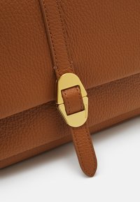 Borsa a tracolla in pelle marrone con finitura testurizzata, caratterizzata da un accento in metallo dorato con fibbia e una tracolla piatta.