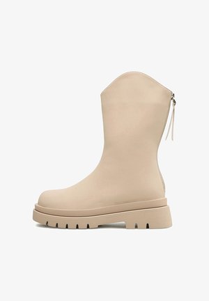 Beżowy skórzany but do połowy łydki z masywną podeszwą i tylnym suwakiem, z zaokrąglonym noskiem i bieżnikowaną podeszwą zapewniającą przyczepność.