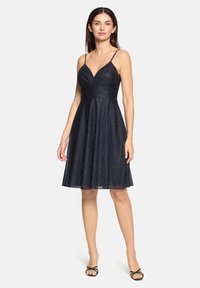 Robe bleu marine avec texture scintillante, corsage ajusté et jupe évasée, dotée de fines bretelles et d'un décolleté en V. Longueur mi-mollet.