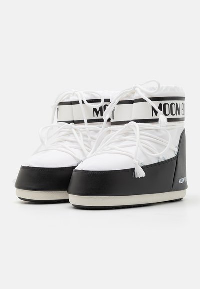 Witte en zwarte enkellaarzen hebben een gewatteerde kraag, een gestructureerde rubbersole, een contrasterende band en decoratieve kwastjes aan de veters.