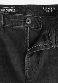 Czarne dopasowane dżinsy z zamkiem błyskawicznym, metalowym guzikiem i przednimi kieszeniami. Gładka tekstura denimu z subtelnymi detalami szwów.