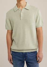 Kortärmad pikétröja i ljusgrönt trikåtyg med klassisk krage och tre krämfärgade knappar, kombinerad med blå jeans.