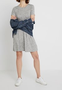 Robe courte à manches courtes rayée grise avec une jupe évasée, associée à une chemise en denim bleue nouée à la taille et des baskets blanches.
