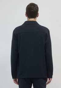 Camicia a maniche lunghe blu navy con colletto appuntito, vestibilità rilassata e yoke posteriore singolo. Tessuto morbido, design minimalista e senza parti metalliche visibili.
