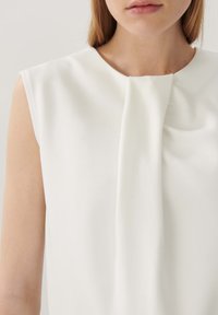 Weißes ärmelloses Top aus glattem Stoff, das ein verdrehtes Detail am Halsauschnitt und ein klares, minimalistisches Design aufweist.