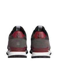 Baskets grises et marron avec un dessus texturé, affichant un logo bien visible sur le talon et des perforations pour la breathabilité. Accents de semelle blanche.