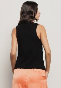 Top nero senza maniche in tessuto a costine, con collo alto e silhouette aderente. Abbinato a pantaloni in satin pesca con dettagli ricamati.