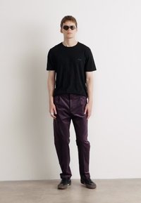 T-shirt en coton noir, pantalon violet avec une finition brillante, porté avec des lunettes de soleil sombres et des chaussures noires. Design simple, sans motifs visibles.