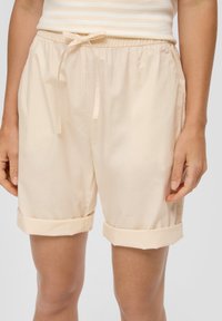 Jasno beżowe szorty bawełniane z elastycznym pasem w talii, sznurkiem do regulacji z przodu oraz podwiniętymi mankietami. Gładka tekstura i prosty design.