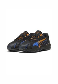 Zapatillas deportivas negras con parte superior de malla, acentos en naranja y azul, cierre de cordones y suela de goma texturizada con patrones de tracción.