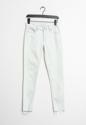 Jeans ajustados de denim de lavado claro con dobladillo deshilachado, que cuentan con un diseño tradicional de cinco bolsillos y un cierre de botón y cremallera.