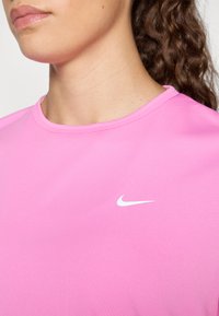 Ručno peta Nike sportska majica u ružičastoj boji s okruglim izrezom i malim bijelim Swoosh logotipom na gornjem lijevom dijelu prsnog koša. Glatka, lagana tkanina.