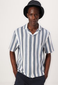 Camisa de botones de manga corta en rayas azul claro, azul marino y crema. Fabricada en tejido tejido con un acabado texturizado. Diseño de cuello tipo campamento.