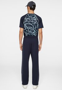 Marinblå träningsklädsel som består av en kortärmad skjorta med ett ljusblått abstrakt mönster på baksidan och matchande byxor med sidostripes.