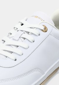 Adidași din piele albă cu șireturi albe, ochiuri aurii și un logo subtil Tommy Hilfiger pe limba și marginea tălpii.