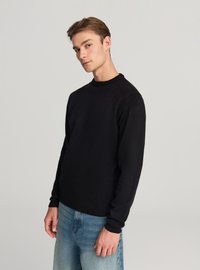 Maglione nero con scollo a girocollo, tessitura a coste e maniche lunghe, abbinato a jeans di denim azzurro chiaro.