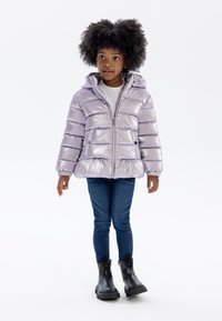 Doudoune lavande avec un matelassage horizontal, capuche, fermeture éclair frontale et poches latérales, associée à un jean bleu et des bottes noires.