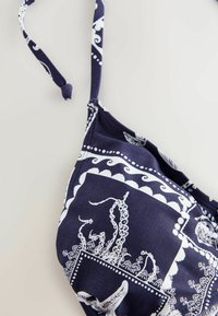 Haut de bikini bleu marine avec motif blanc pieuvre et algues, avec une bretelle nouée sur l'épaule sur fond neutre.