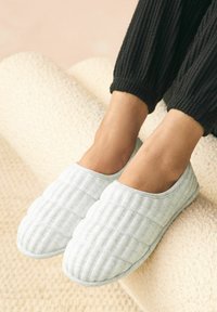 Lysegrå, quiltede slippers med blød tekstur og rund form, der har en åben rygdesign og minimalistiske sømme.