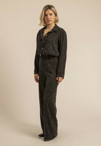 Blouse à manches longues noir et blanc à carreaux avec un col, associée à un pantalon large taille haute assorti. Texture lisse.