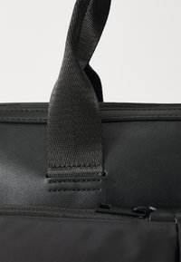 Sort lædertaske med en struktureret overflade, holdbart stofhåndtag og en lynlås i toppen. Slank, minimalistisk design.