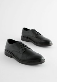 Zapatos de vestir de cuero negro con un acabado liso, punta redondeada, cordones en la parte frontal y tacón bajo. Diseño minimalista con detalles de costura sutiles.