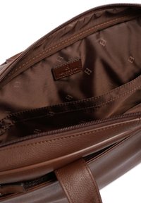 Bruine leren handtas met een gladde textuur, ritssluiting en een gelabelde leren tag aan de binnenkant. Het interieur heeft een donkerbruine voering met een subtiel patroon.