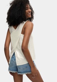 Licht beige mouwloze top met een crossover achterkant, gecombineerd met denim shorts met een rafelige zoom. Soepele stoftexture.