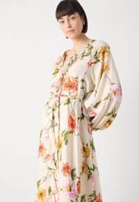 Abito avvolgente floreale in tessuto crema con grandi fiori rosa, arancio e gialli. Presenta un colletto arricciato e lunghe maniche a palloncino.