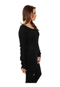 Pull en tricot noir à coupe décontractée, avec un col rond, des manches longues et un design texturé, atteignant la longueur des hanches.