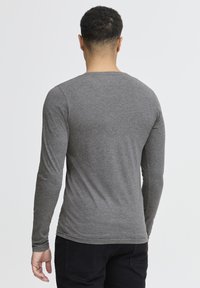 Grå langærmet skjorte lavet af et blødt, strækbart stof. Rund hals, tætsiddende stil med en glat tekstur og minimal detaljer.