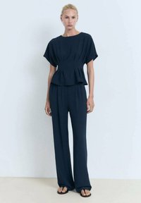 Námořnický dvoudílný outfit s boxy, skládacím topem s krátkými rukávy a kalhotami s širokými nohavicemi. Tkanina vypadá texturovaně s volným střihem.