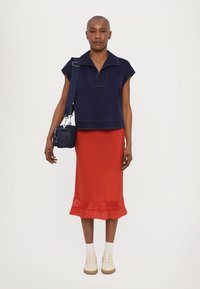 Navy short-sleeve top with a collar, paired with a red midi skirt featuring a ruffled hem. Footwear is beige sneakers. Small bag included.