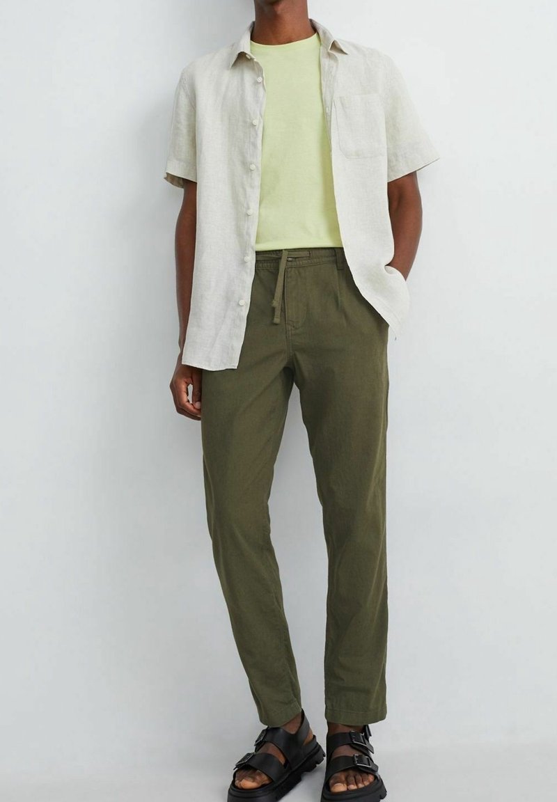 Lniana koszula z krótkim rękawem w jasnobeżowym kolorze, zestawiona z żółtą koszulką i oliwkowozielonymi spodniami; czarne sandały z paskami.