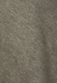 Tejido texturizado en verde oliva con sutiles patrones de tejido diagonal. Material suave que muestra una apariencia ligeramente jaspeada.