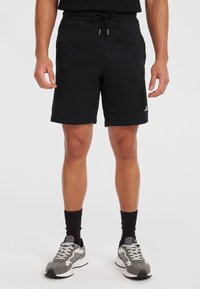 Black athletic shorts made of soft fabric, featuring a drawstring waistband, side pockets, and a rolled hem. Worn with gray sneakers and black socks.
