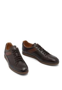 Un paio di sneaker casual in pelle marrone scuro con lacci e una striscia marrone chiaro sul lato, presentate su uno sfondo bianco.