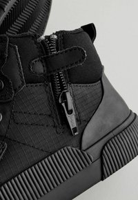 Schwarze High-Top-Sneaker aus Textil mit Reißverschluss, strukturierten Einsätzen und einer Gummisohle mit horizontalen Rillen.
