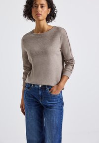Beige gebreide trui met een ronde hals en geribde manchetten, gecombineerd met blauwe wijde denim jeans met zijzakken en een knoopsluiting.