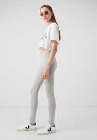 Gray leggings with a smooth texture, paired with a white cropped t-shirt featuring a blue shell design, and white sneakers with black accents.