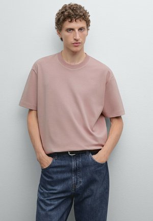 Hellrosa Baumwoll-T-Shirt mit kurzen Ärmeln und rundem Ausschnitt, kombiniert mit blauen Jeans. Schlichte, lockere Passform. Mininale Details.
