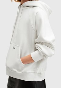 Witte hoodie gemaakt van zachte stof, met een voorzak, capuchon met trekkoord en geribbelde manchetten. Eenvoudig ontwerp met minimale accenten.