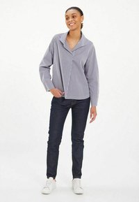 Chemise rayée à manches longues en bleu marine et blanc, avec un col et une coupe décontractée, associée à un jean en denim foncé et des baskets blanches.