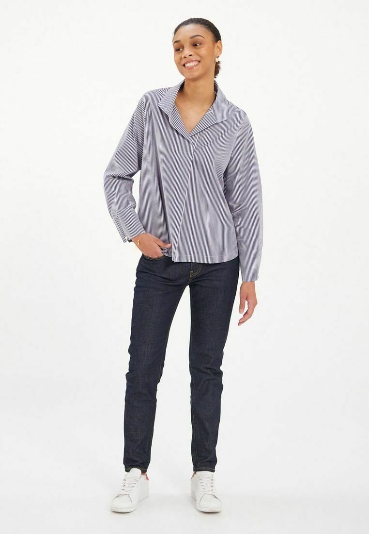 Chemise rayée à manches longues en bleu marine et blanc, avec un col et une coupe décontractée, associée à un jean en denim foncé et des baskets blanches.