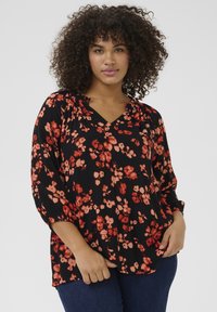 Blusa negra con patrón floral rojo, escote en V y mangas tres cuartos, hecha de un tejido ligero con una sutil textura.