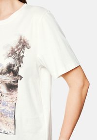 Witte katoenen t-shirt met korte mouwen, voorzien van een grafische print van bomen en water, met zachte aardetinten en subtiele texturen.
