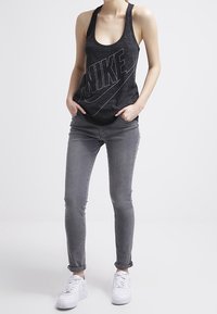 Svart Nike linne med en djärv logotyp, kombinerat med grå skinny jeans och vita sneakers. Linnet har en rundad halsringning och är ärmlöst.